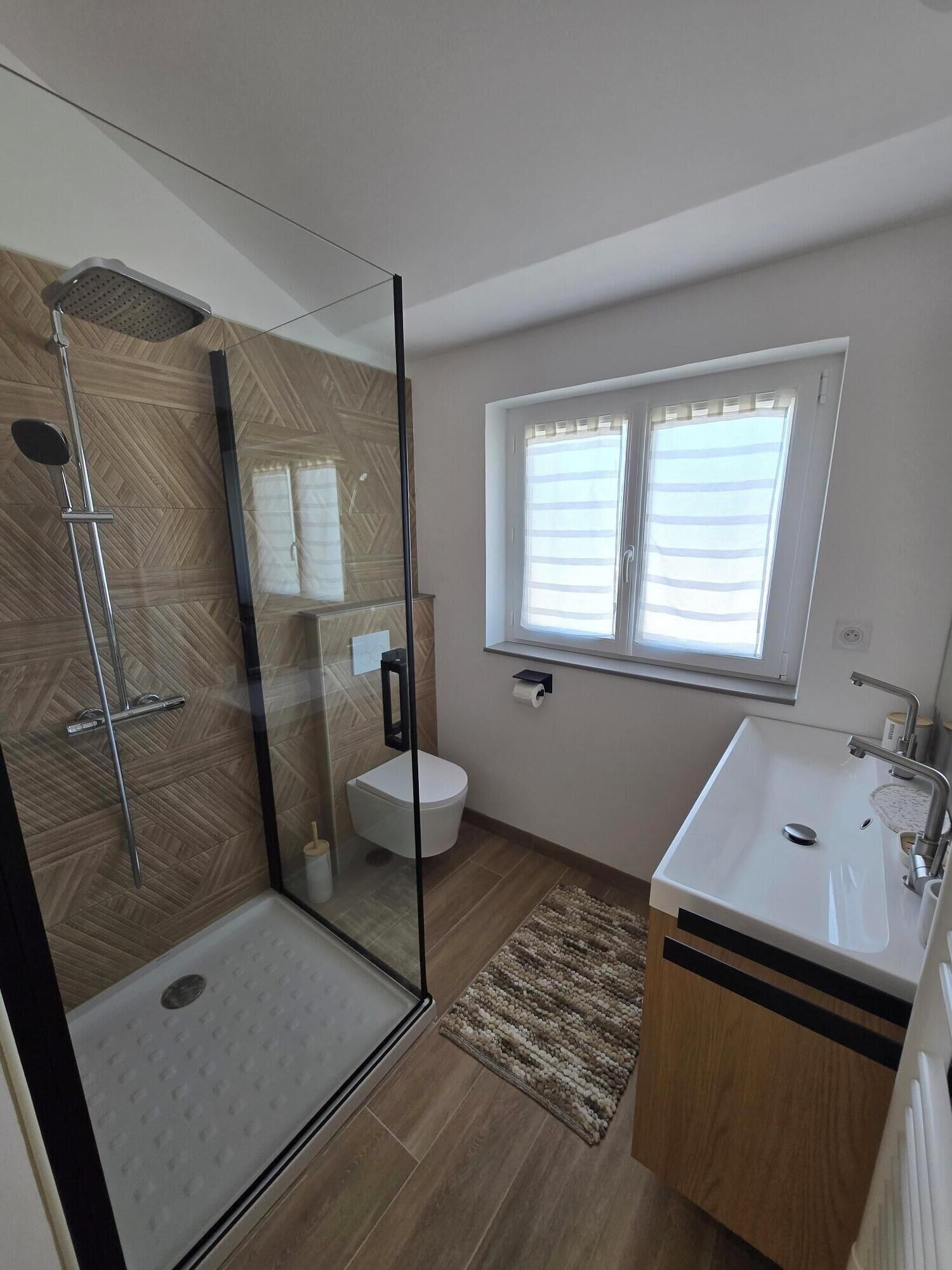 Une salle de bain moderne avec une douche à parois de verre, des toilettes, un lavabo et une fenêtre.