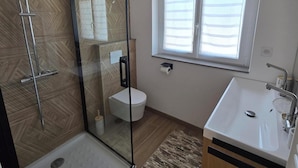 Un baño moderno con ducha de vidrio, inodoro, lavamanos y ventana.