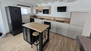 Una cocina moderna con un refrigerador negro, un microondas y un lavavajillas. Hay una mesa de madera con dos taburetes.