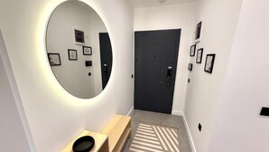 A hallway with a round mirror, a bench, a rug, and a door. - OLİVE SUİTE 2+1 Family Apartment - 200m Walking Distance to the Beach (Kemer)