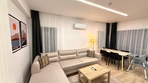 A modern living room with a sofa, coffee table, dining table, and chairs. - OLİVE SUİTE 2+1 Family Apartment - 200m Walking Distance to the Beach (Kemer)