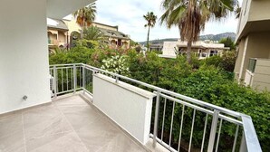 A balcony with a white railing, a tiled floor, and a view of neighboring buildings and greenery. - OLİVE SUİTE 2+1 Family Apartment - 200m Walking Distance to the Beach (Kemer)
