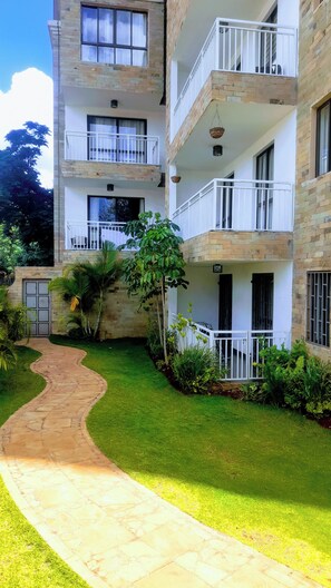 A multi-story building with balconies, a paved pathway, and a well-maintained garden. - Luxurious 2 Bedroom Duplex Apartment in Kilimani, Nairobi (Nairobi)