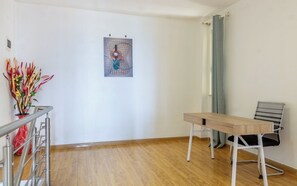 Een kamer met een houten vloer, een bureau met stoel, een metalen leuning en een kunstwerk aan de muur.