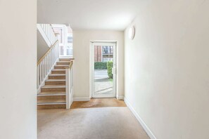 A hallway with a carpeted floor, a white door, and a staircase with wooden railings. - Host & Stay | Linden Homes (Redhill)
