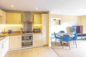 A modern kitchen with built-in appliances, a dining area with blue chairs, and a large window. - Host & Stay | Linden Homes (Redhill)