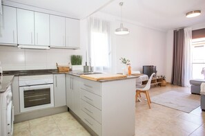 A modern kitchen with white cabinets, a built-in oven, a wooden countertop, and a dining area with a table and chairs. - Laura.Modern, sunny apartment in quiet area (Lloret de Mar)