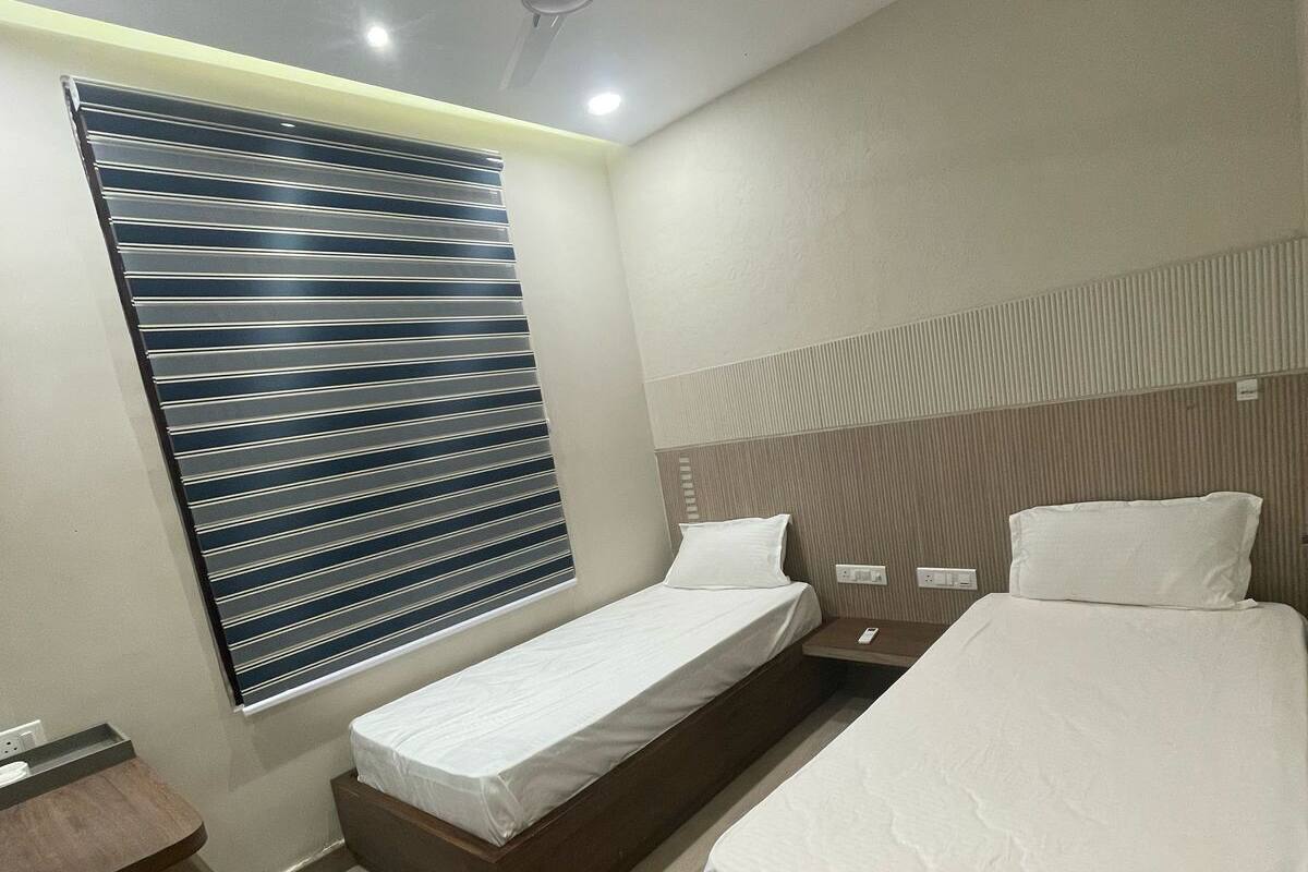 A hotel room with two beds, a desk, a ceiling fan, and a window with blinds.