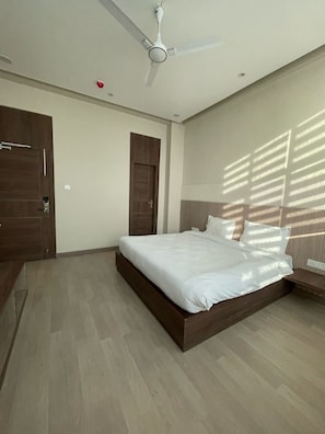 A modern bedroom with a bed, a ceiling fan, wooden doors, and a window with blinds. - Hotel Aman Paradise (Kanpur)