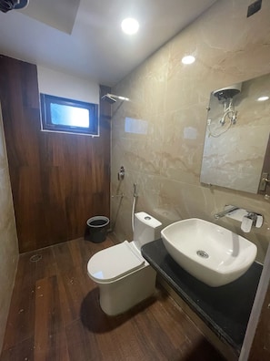 A bathroom with a wooden floor, a white toilet, a white sink, a shower, and a mirror. - Hotel Aman Paradise (Kanpur)