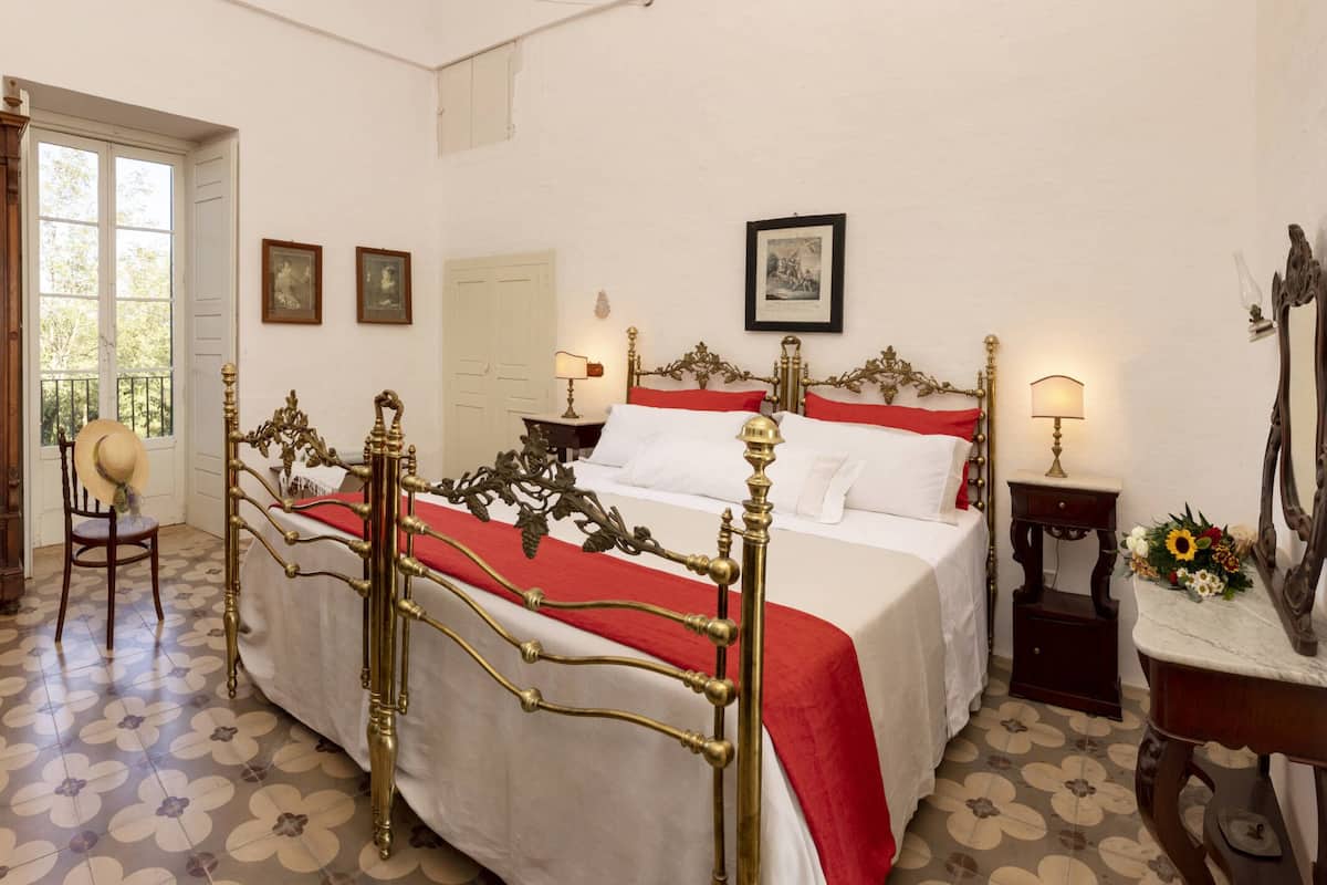 Une chambre à coucher comprenant un lit, une chaise, une table de chevet, un miroir et une porte.
