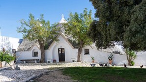 A white building with a stone roof, surrounded by trees and a grassy area. - Masseria Tagliente (Martina Franca)