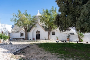 A white building with a stone roof, surrounded by trees and a grassy area. - Masseria Tagliente (Martina Franca)