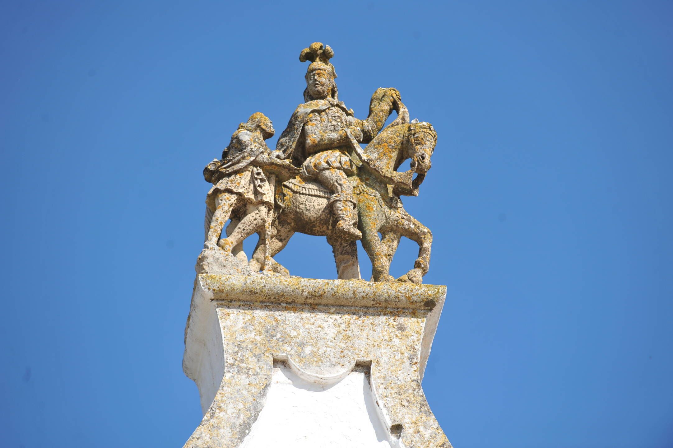 Un monumento de piedra con una figura a caballo, flanqueado por dos figuras más pequeñas, frente a un cielo azul despejado.