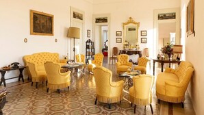 A spacious living room with yellow upholstered chairs, a patterned floor, and a large mirror. - Masseria Tagliente (Martina Franca)