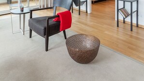 Moderni hotellihuone, jossa on suuri liukuovi, valkoisilla lakanoiden peitetty sänky, pieni pöytä, jossa on punainen maljakko, ja punaisella heittotyynyllä koristeltu tuoli.