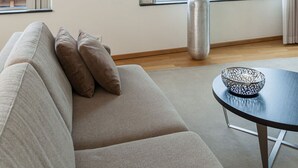 Moderni olohuone, jossa on sohva, sohvapöytä, kuivakukkia sisältävä maljakko ja seinällä oleva kehystetty kuva.