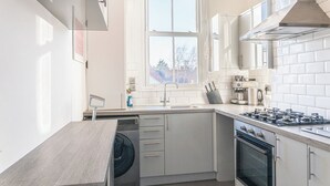 Une cuisine moderne équipée d’un lave-vaisselle encastré, d’une cuisinière à gaz et d’une fenêtre laissant entrer la lumière naturelle.