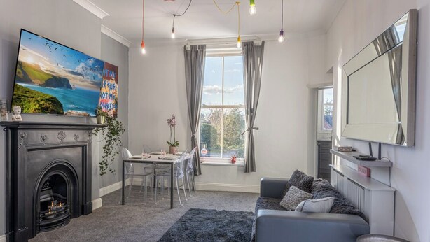 Un salon moderne doté d’une cheminée, d’un coin repas et d’une grande fenêtre agrémentée de rideaux.