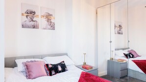 Une chambre à coucher moderne avec un lit, des tables de chevet, un miroir et des œuvres d’art accrochées au mur.