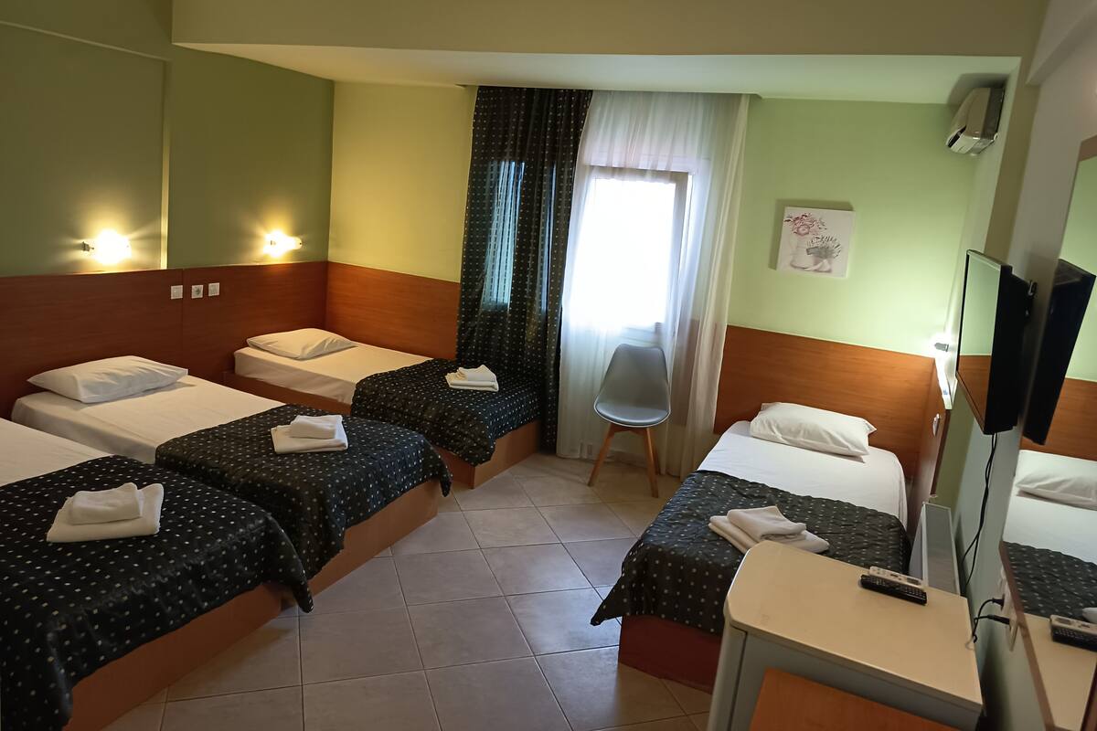 Une chambre d’hôtel avec quatre lits simples, un bureau avec une télévision et une chaise.
