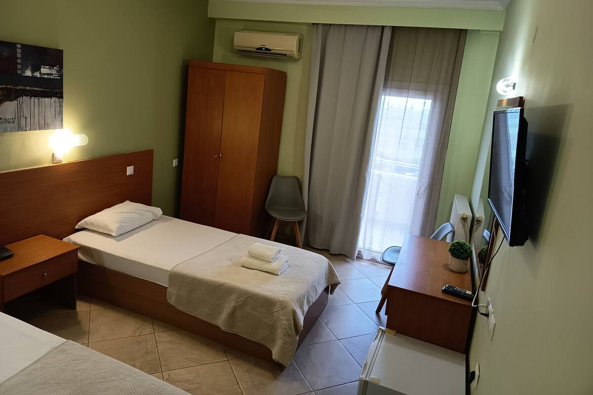 Une chambre d’hôtel équipée d’un lit, d’un bureau, d’une armoire, d’une télévision et d’une fenêtre avec des rideaux.