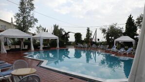 Una piscina con lettini e tavoli, circondata da alberi e coperta da tende bianche.