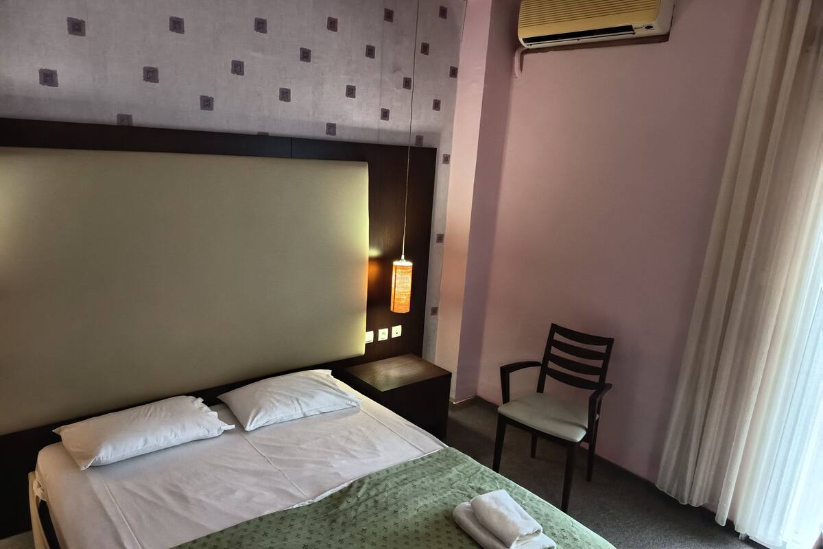 Une chambre d’hôtel équipée d’un lit, d’une chaise, d’un climatiseur et d’une lampe fixée au mur.
