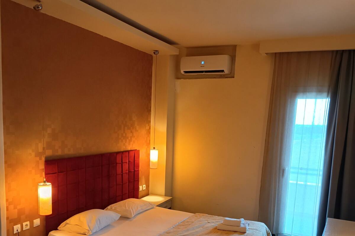 Une chambre d’hôtel comprenant un lit, des tables de chevet, un bureau, une chaise, un appareil de climatisation et une fenêtre avec des rideaux.