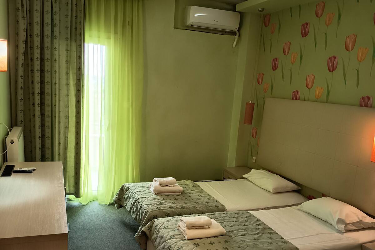 Une chambre d’hôtel avec deux lits, un bureau, une chaise et un appareil de climatisation.