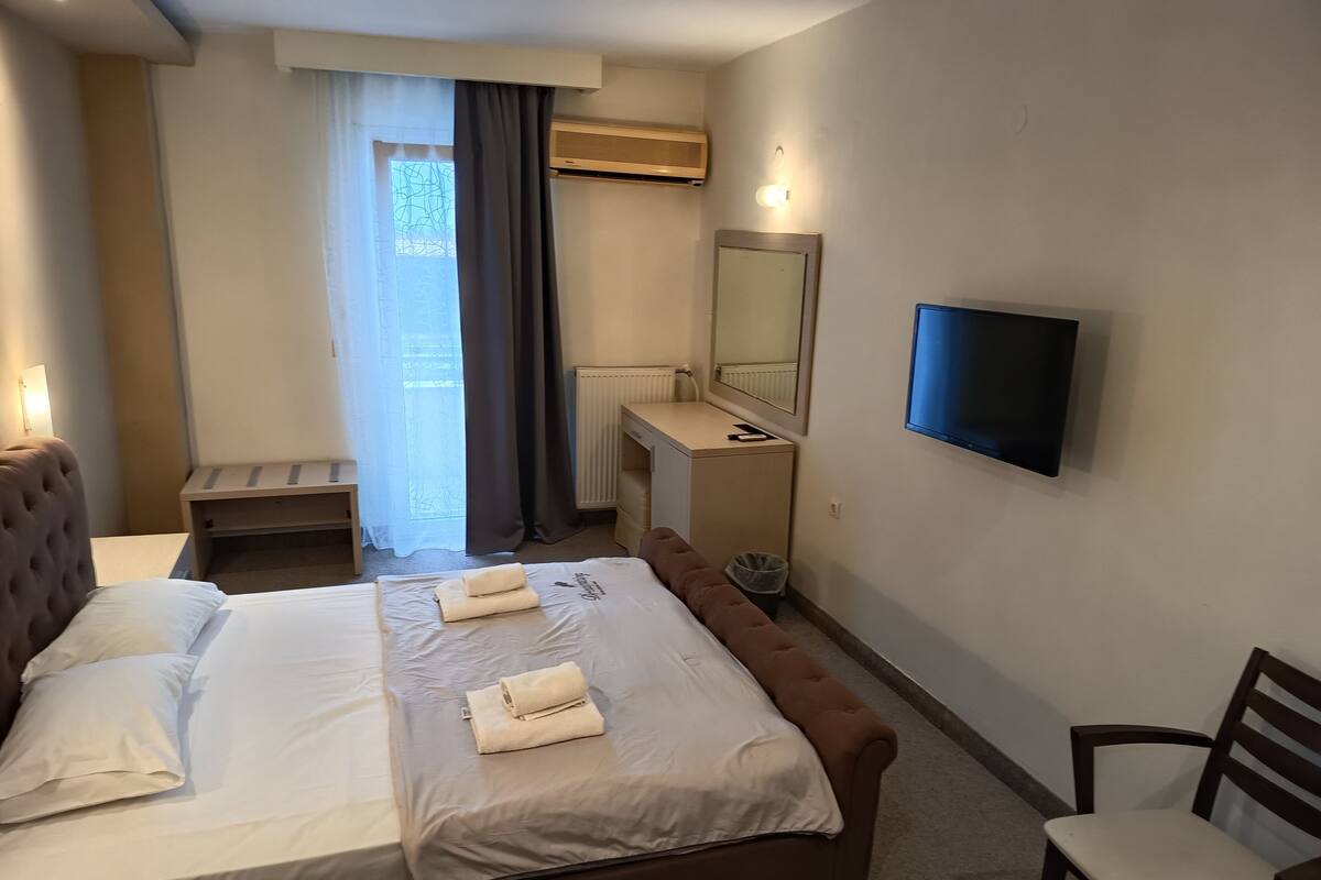 Une chambre d’hôtel équipée d’un lit, d’un bureau, d’une chaise, d’une télévision et d’une fenêtre avec des rideaux.