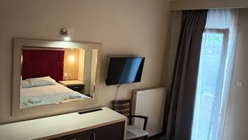 Habitación de hotel con cama, escritorio, silla, televisor, ventana con cortinas y radiador.