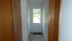 Un couloir avec des portes en bois, un sol carrelé et une porte blanche au fond.