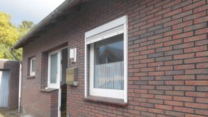 Un bâtiment en briques avec une porte d’entrée, deux fenêtres et une boîte aux lettres.