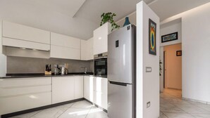 Una cocina moderna con armarios blancos, un refrigerador de acero inoxidable y una encimera con electrodomésticos.