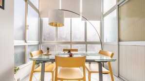 Un comedor con mesa de vidrio, sillas amarillas y una lámpara colgante.