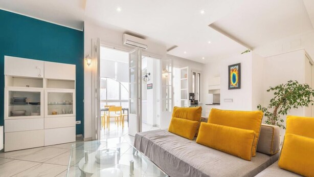 Una sala moderna con un sofá, una mesa de centro de vidrio y un armario blanco.