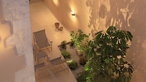 A sunlit outdoor patio with a seating area, plants, and wall-mounted lights. - Moshoviti Residence (Rethymno)