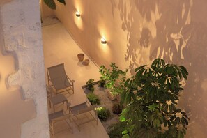 A sunlit outdoor patio with a seating area, plants, and wall-mounted lights. - Moshoviti Residence (Rethymno)