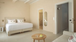 A bedroom with a bed, a round wooden table with a glass and a bowl of fruit, and a door leading to another room. - Moshoviti Residence (Rethymno)
