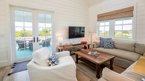 A living room with a TV, sofa, coffee table, and a balcony with outdoor furniture.