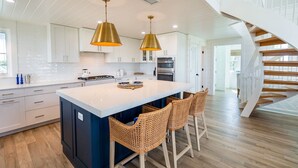 A modern kitchen with a central island, two pendant lights, and a spiral staircase.