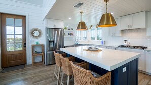 A modern kitchen with a large island, stainless steel appliances, and wicker bar stools.