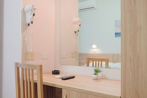 A room with a wooden desk, a chair, a hairdryer, a remote control, a small plant, and a mirror reflecting a bed and a nightstand. - Hotel Blue Ribbon (Rivazzurra)