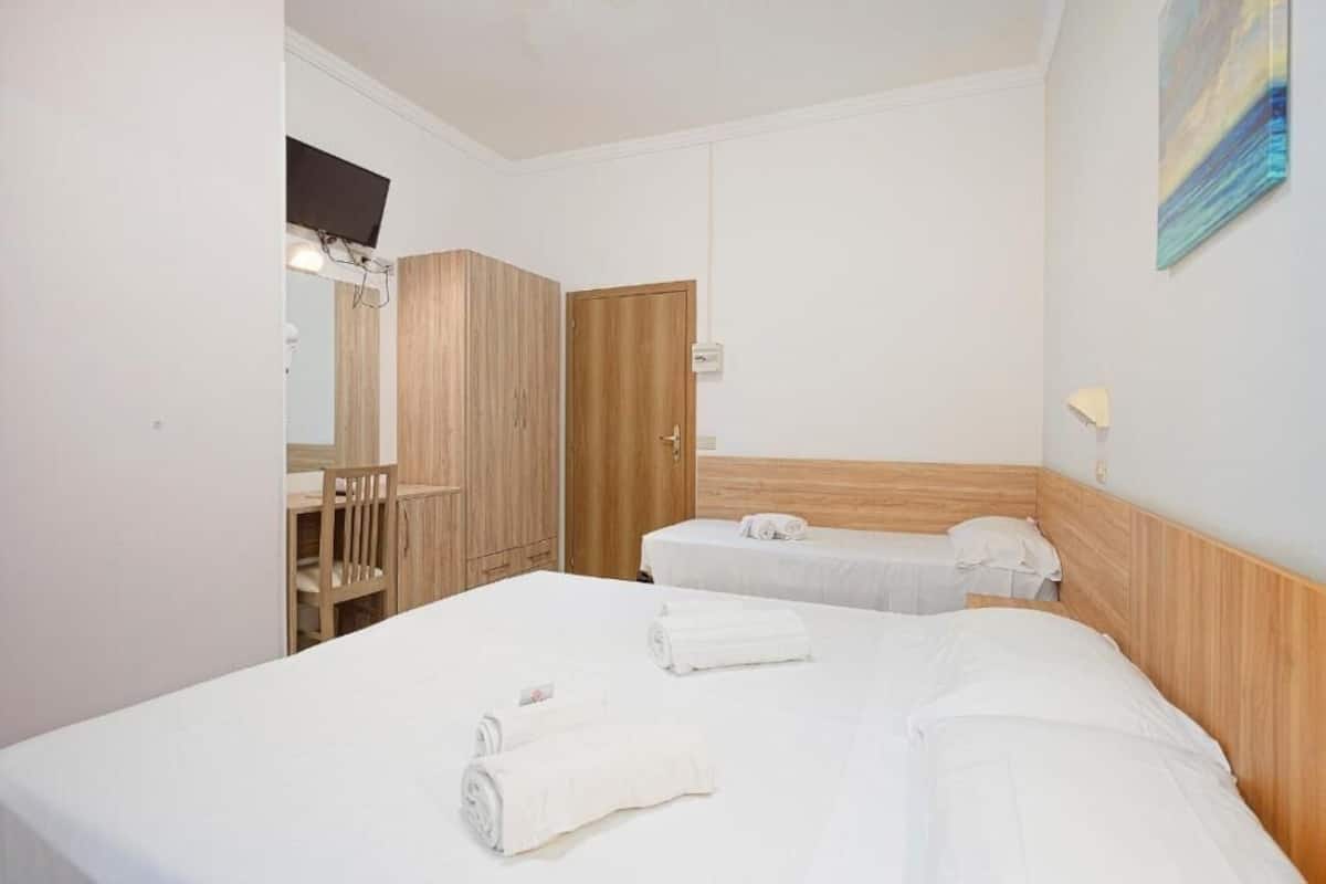 A hotel room with two beds, a desk, a chair, a wooden wardrobe, and a painting on the wall.