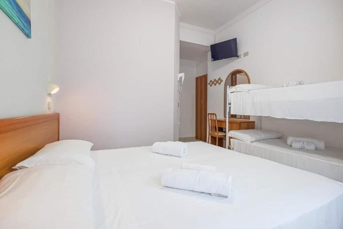 A hotel room with a bed, a TV mounted on the wall, a mirror, and a wooden chair.