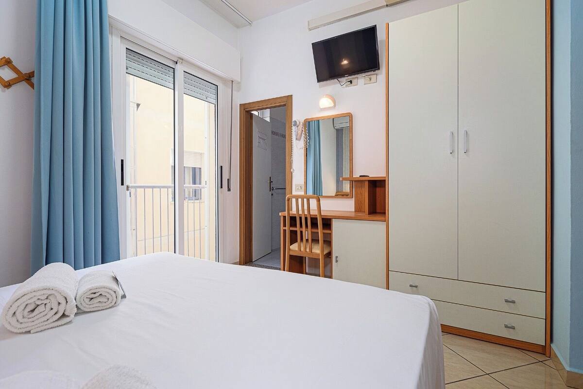 A hotel room with a bed, a desk, a TV, and a wardrobe.