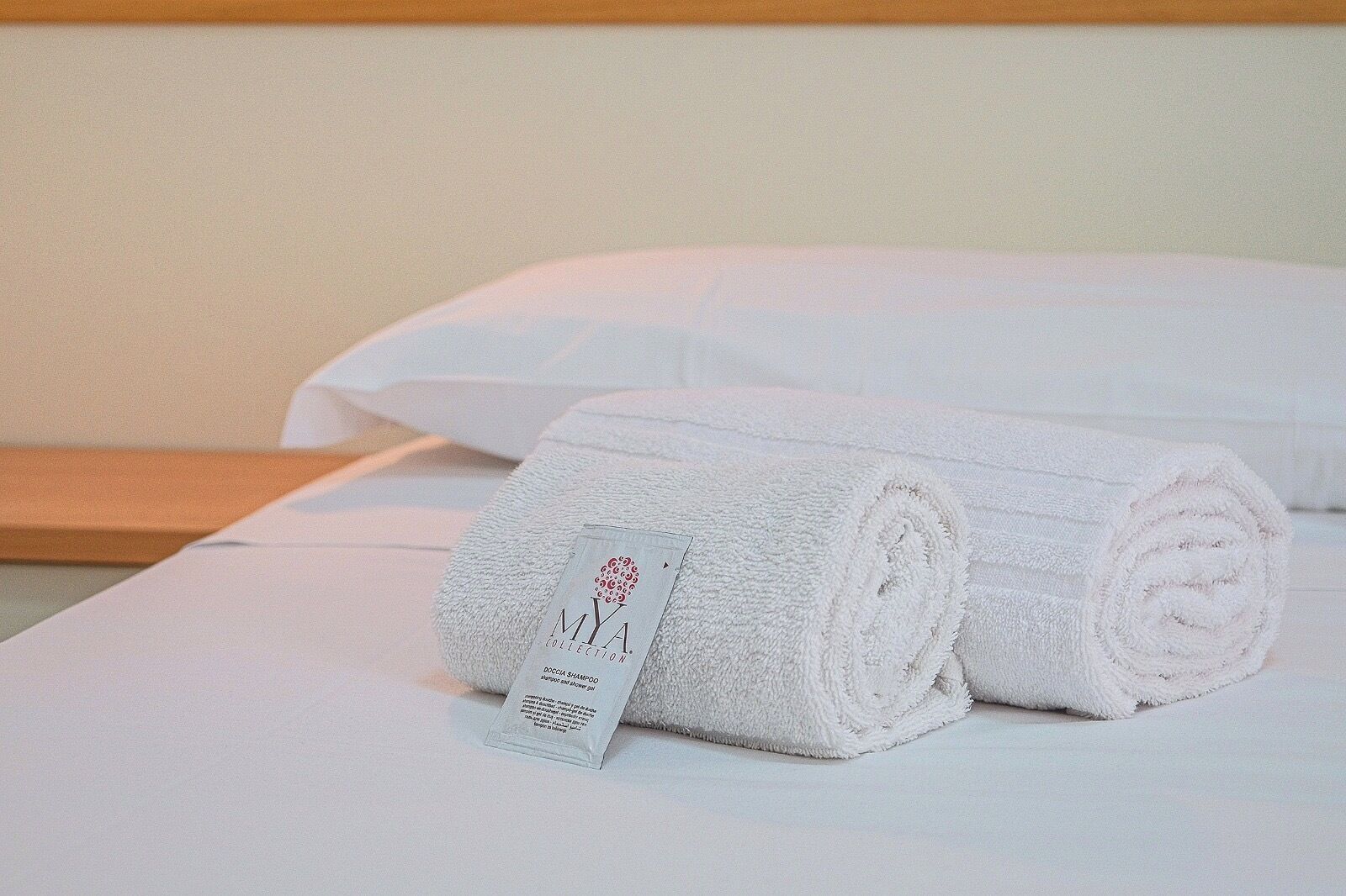 A neatly made bed with white linens and a rolled towel with a tag.