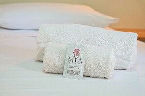 Neatly folded white towels and a shampoo bottle on a bed.