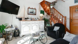 A living room with a TV, a sailboat model, a staircase, and a black chair. - Apartment "Gîte Etienne Marie" with Private Terrace (Le Crotoy)